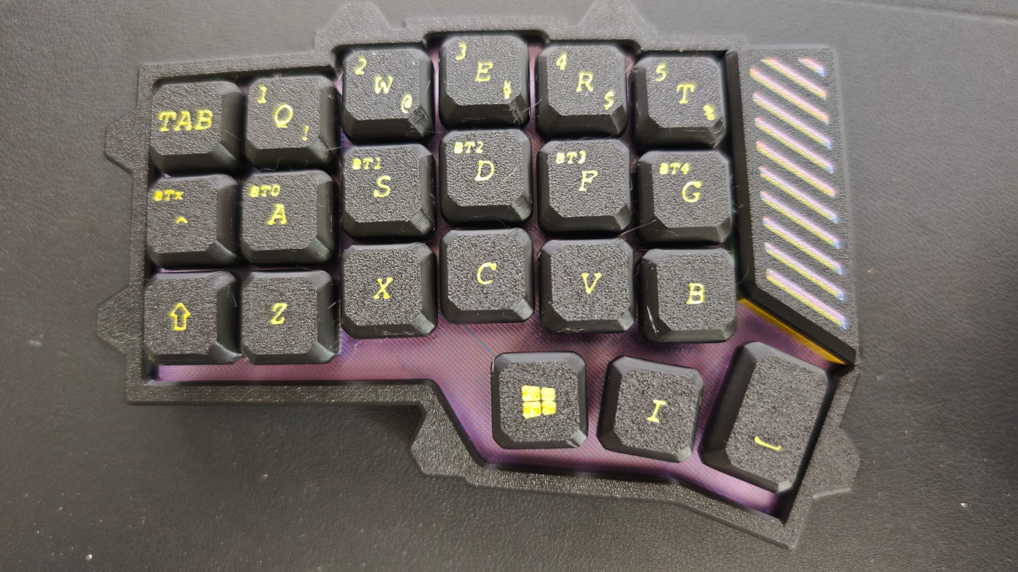Close-up of the assembled left half with thick 3D-printed keycaps installed, gold legends on black keys over an iridescent purple case.